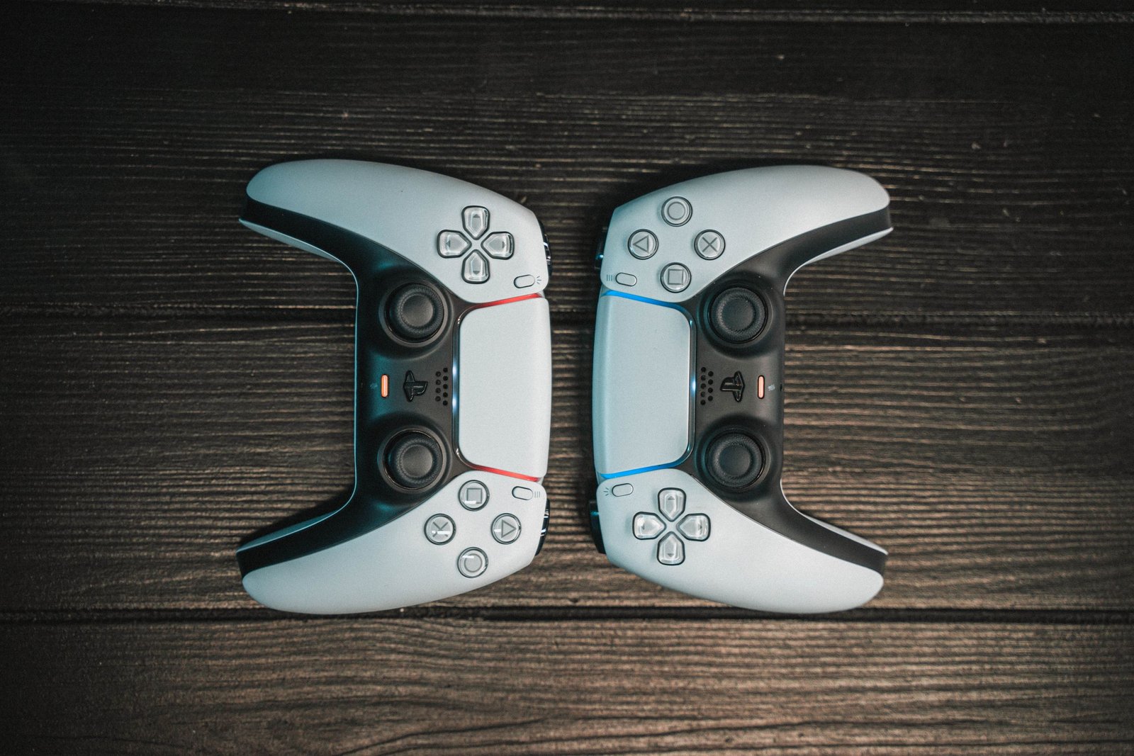 Two gaming controllers aligned symmetrically on a dark wooden surface, top view.